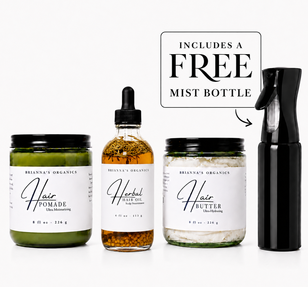 Four Brianna's Organics hair care products arranged on a white background: a green pomade jar, an amber herbal oil dropper bottle, a white butter jar, and a black mist bottle. A text callout says it includes a free mist bottle.