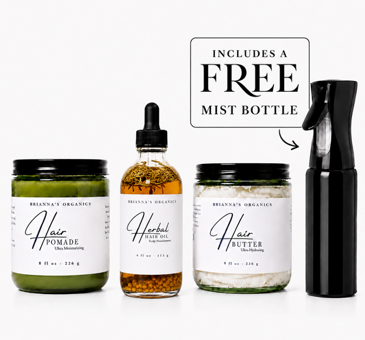 Four Brianna's Organics hair care products arranged on a white background: a green pomade jar, an amber herbal oil dropper bottle, a white butter jar, and a black mist bottle. A text callout says it includes a free mist bottle.